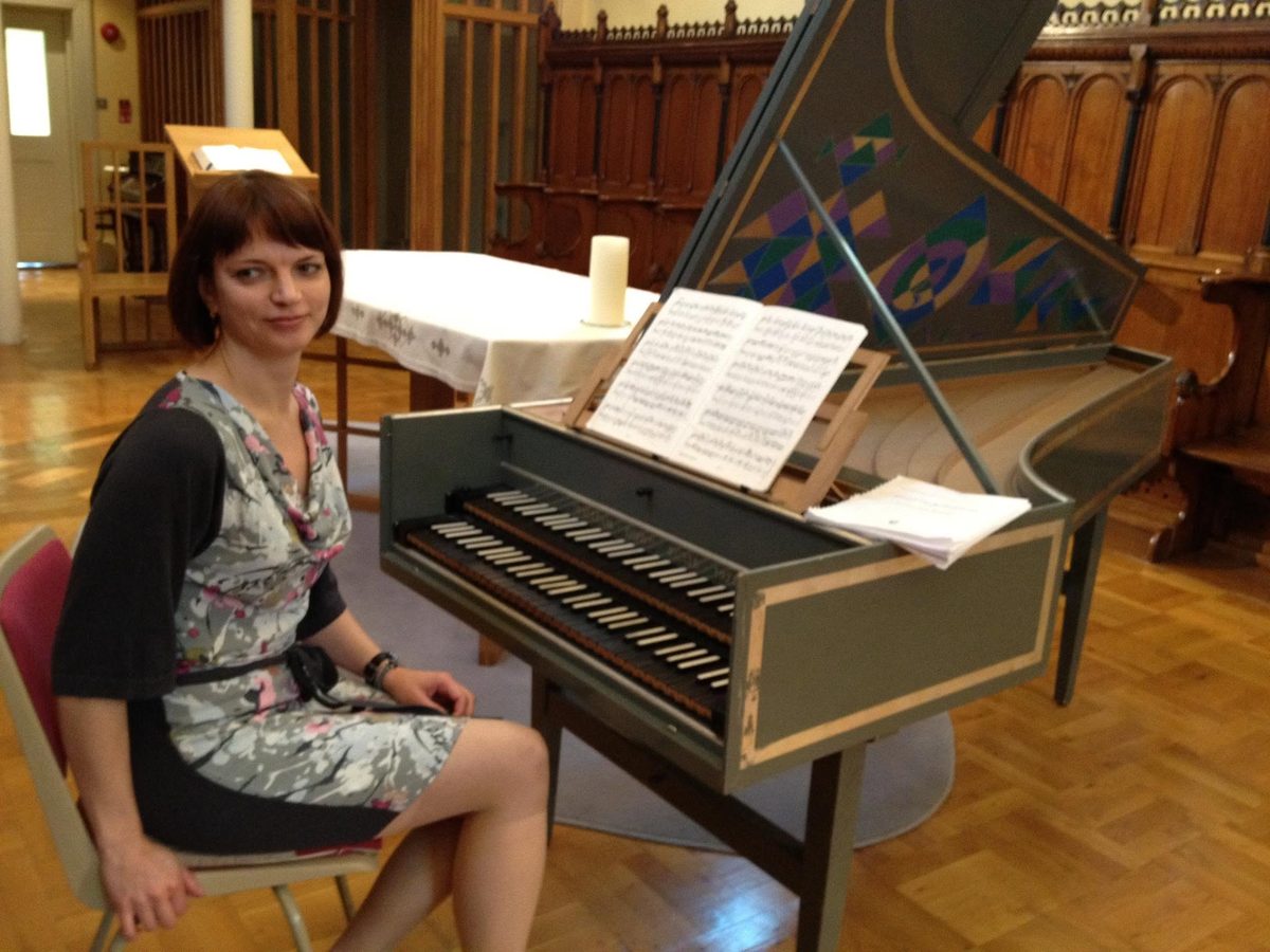 Tetyana seated at a decorated harpsichord, sheet music open on the stand